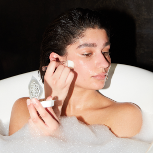 A woman in a bathtub applying Hanacure product to her face