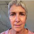 Woman with short gray hair and teal earrings against a neutral background